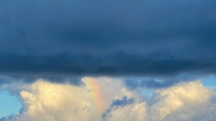 a small rainbow connects dark and white clouds