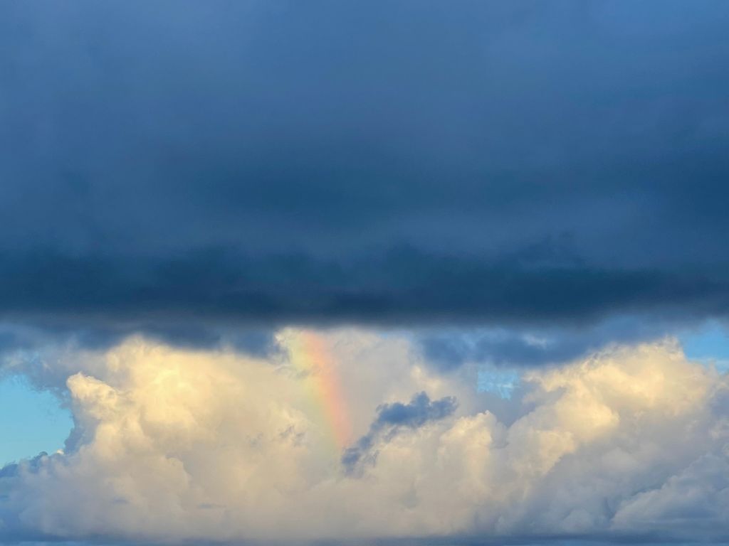 a small rainbow connects dark and white clouds